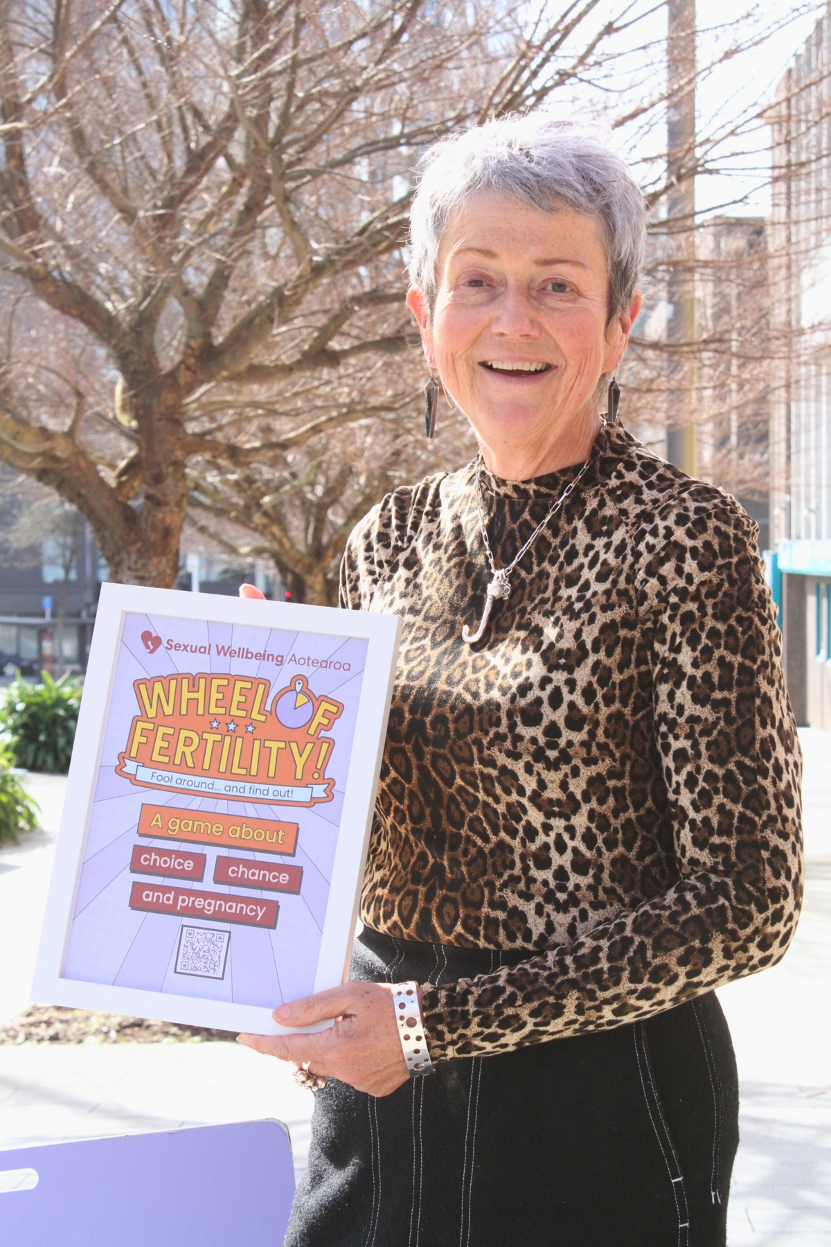 Chief Executive Jackie Edmond holding a poster about the Wheel of Fertility game