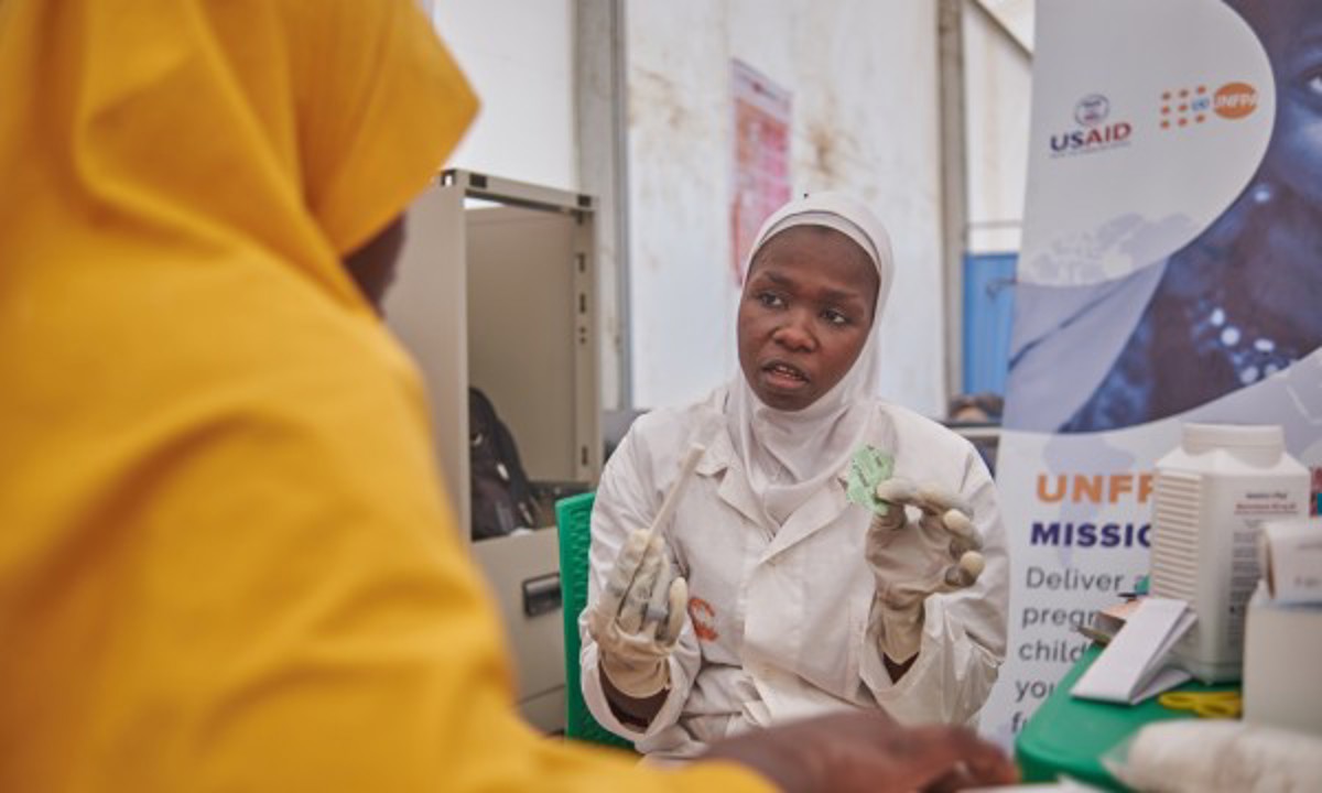 A healthcare worker attends to a mother during an ante natal care visit in UNFPA flood response tent in Bakasi IDP Camp Maiduguri, Borno, Nigeria.